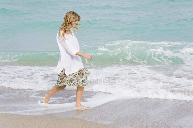 Sorrindo jovem mulher andando na praia com as mãos no cabelo — Fotografia de Stock