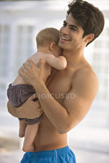 Shirtless young smiling man carrying little son — Stock Photo