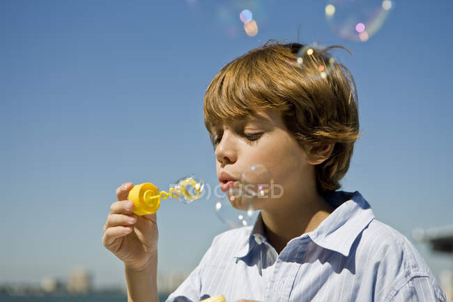 Хлопчик дме бульбашки з бульбашковою паличкою на блакитне небо — стокове фото