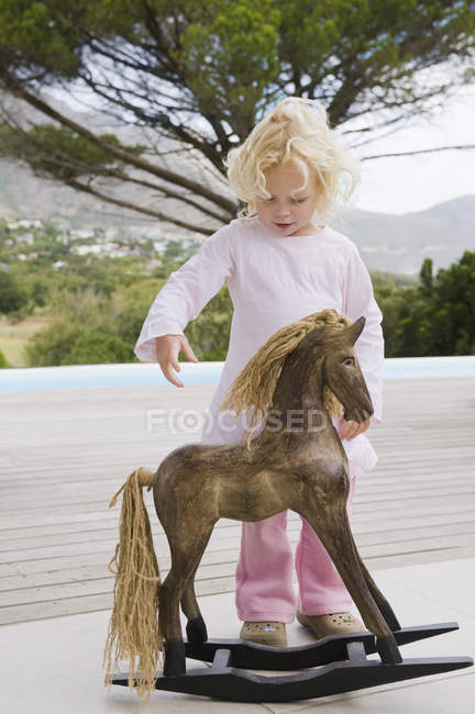 Girl standing near rocking horse outdoors — Stock Photo