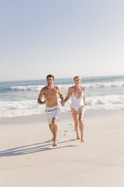 Couple courant sur une plage de sable tenant la main — Photo de stock