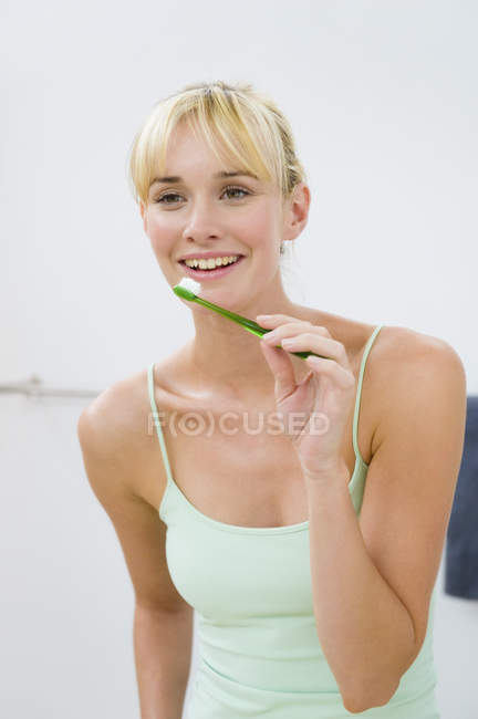 Усміхнена молода жінка тримає зубну щітку у ванній — стокове фото