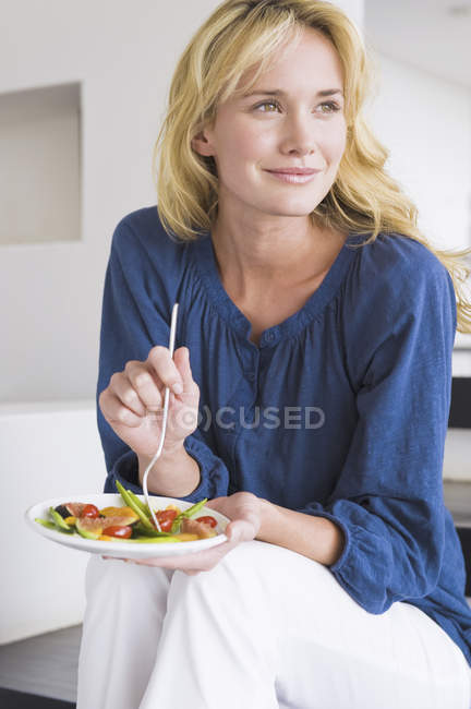 Donna elegante sorridente che tiene il piatto di macedonia di frutta e distoglie lo sguardo — Foto stock