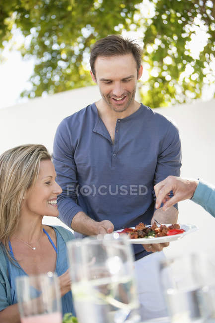Uomo sorridente che serve piatto di cibo durante la festa all'aperto — Foto stock