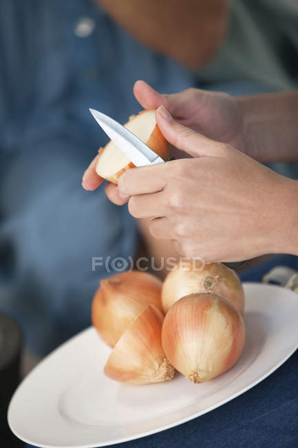 Mani femminili che tagliano cipolle su piatto — Foto stock