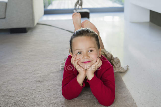 Portrait of smiling little girl lying on carpet at home — Stock Photo