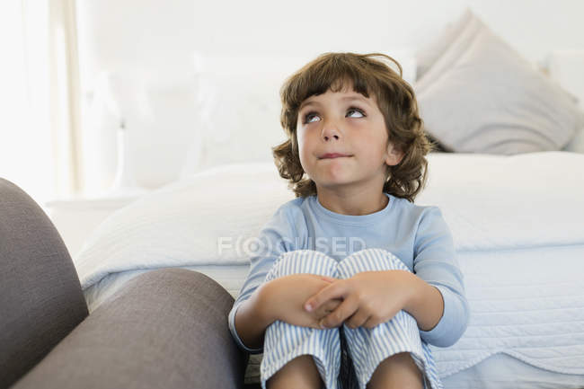 Продуманий маленький хлопчик сидить у ліжку і дивиться вгору — стокове фото