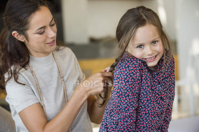 Усміхнена жінка плете волосся своєї дочки — стокове фото