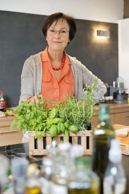 Portrait of woman standing in kitchen with organic herb plant — Stock Photo
