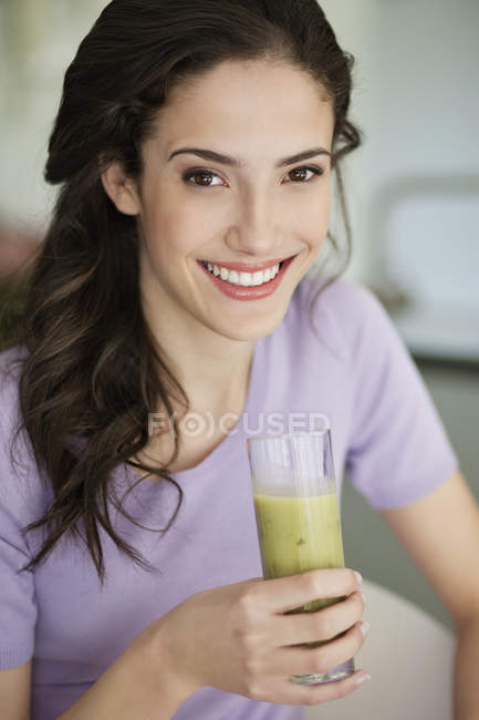 Жінка тримає склянку овочевої смузі і посміхається — стокове фото