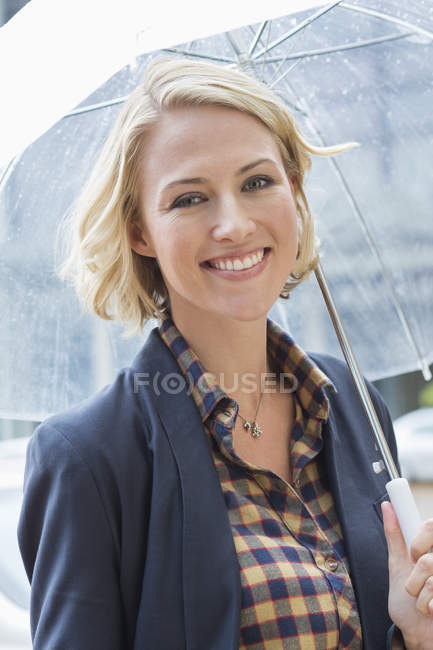 Портрет усміхненої блондинки, що стоїть з парасолькою на відкритому повітрі — стокове фото
