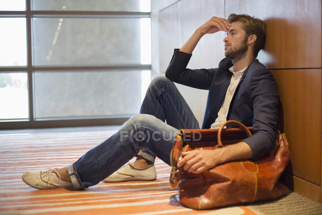 Müder junger Mann lehnt am Flughafen an Wand — Stockfoto
