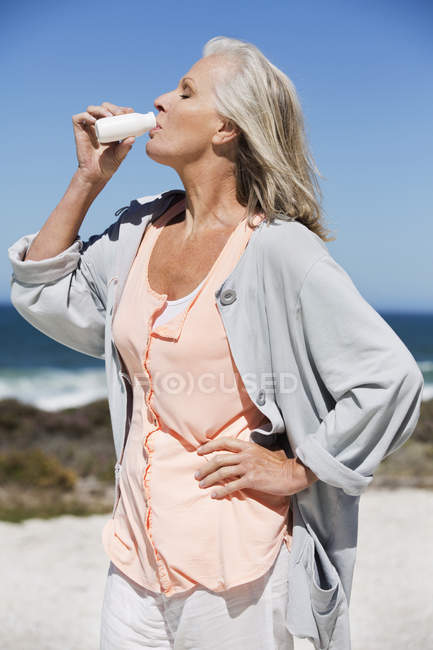 Seniorin genießt probiotischen Drink am Strand — Stockfoto