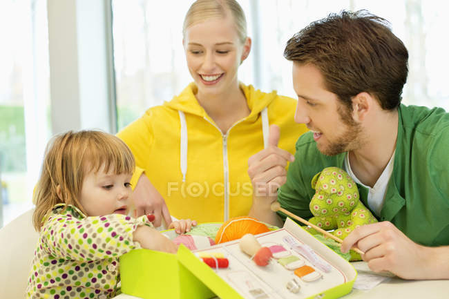 Menina sentada com os pais olhando para a caixa do kit de tricô — Fotografia de Stock