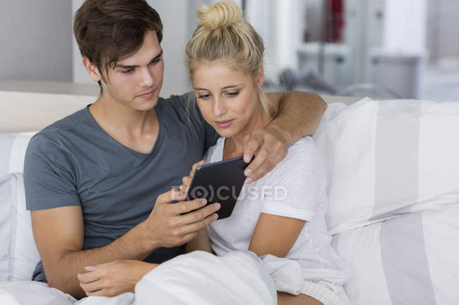 Young embracing couple using digital tablet on bed — Stock Photo