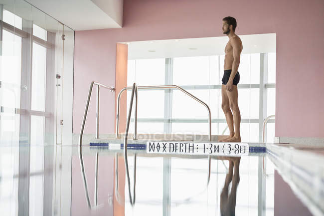 Tall athletic man standing at indoor pool side — Stock Photo