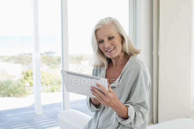 Mulher idosa usando tablet digital e sorrindo em casa — Fotografia de Stock