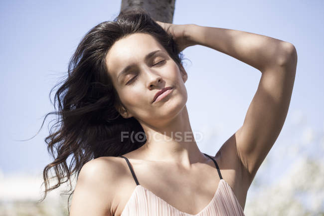 Расслабленная женщина с закрытыми глазами, опирающаяся на ствол дерева — стоковое фото