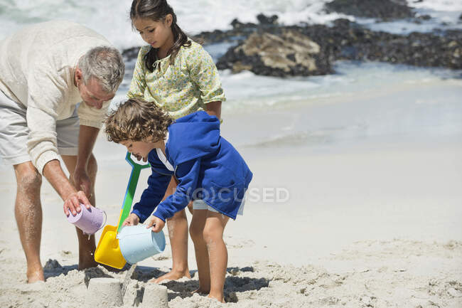 Діти бавляться з дідусем на пляжі. — стокове фото