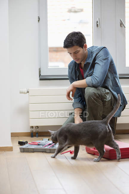 Técnico masculino arreglando caja de herramientas en el suelo con gato - foto de stock