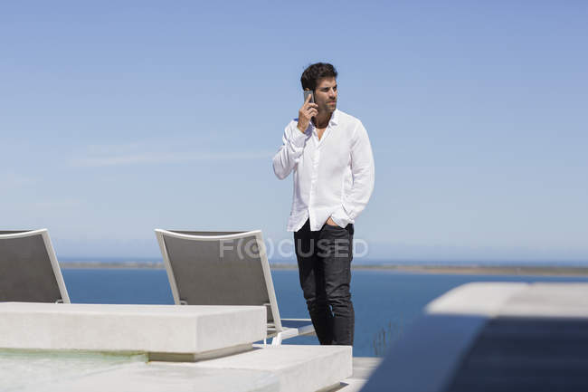 Hombre seguro de sí mismo hablando por teléfono móvil en la terraza en la orilla del lago - foto de stock