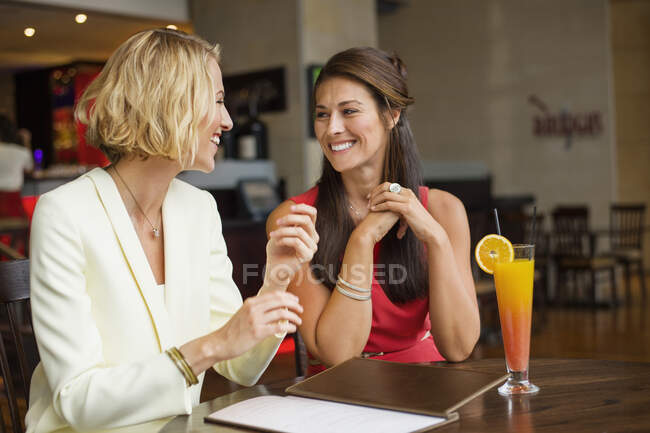 Duas amigas a sorrirem uma para a outra num restaurante. — Fotografia de Stock