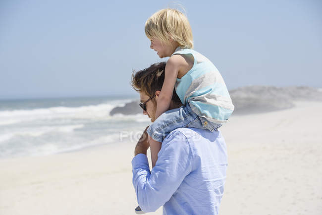 Giovane uomo che porta il figlio sulle spalle sulla spiaggia di sabbia — Foto stock