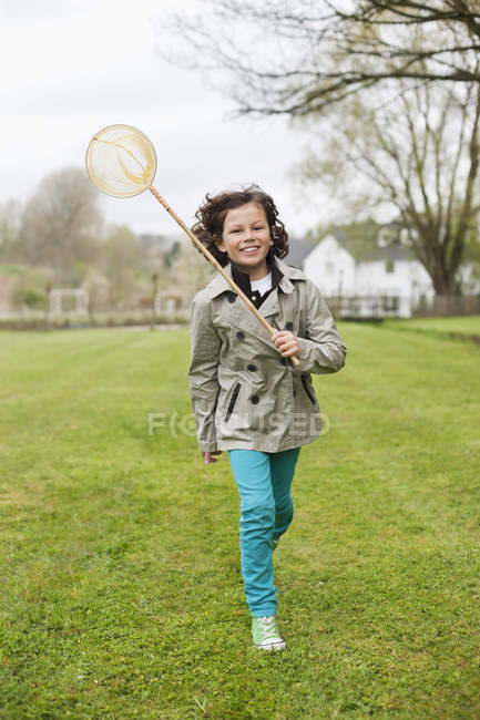 Niño feliz corriendo con una red de mariposas en el campo de otoño - foto de stock