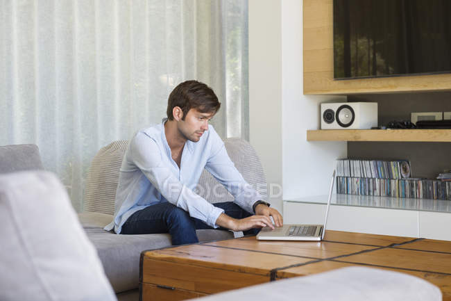 Giovane uomo che utilizza il computer portatile sul divano a casa — Foto stock