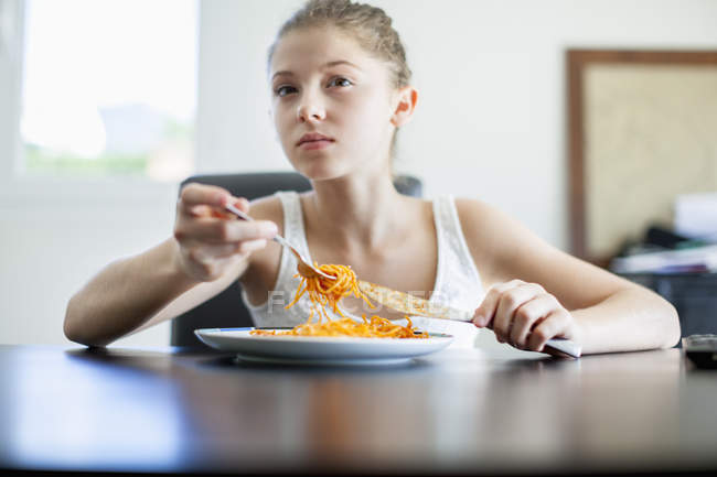 Adolescente comiendo espaguetis en la mesa y mirando hacia otro lado - foto de stock