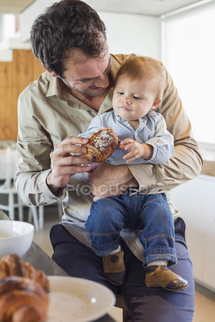 Man feeding bread to his son at a kitchen counter — Stock Photo