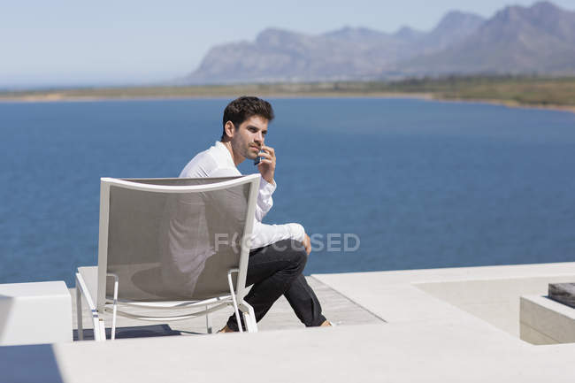 Заботливый человек, сидящий на шезлонге и разговаривающий по мобильному телефону на берегу озера — стоковое фото