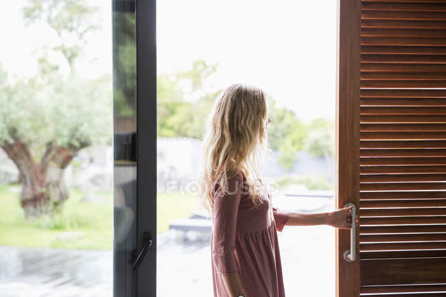 Mulher loira em pé na janela de vidro do terraço — Fotografia de Stock