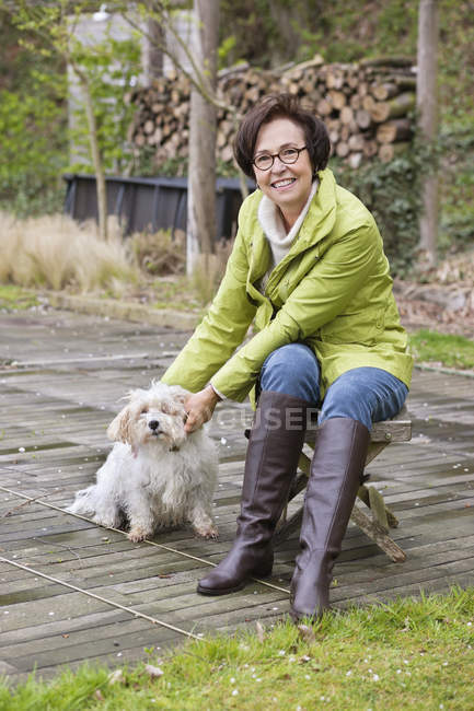Femme assise sur un tabouret en bois à l'extérieur avec chien — Photo de stock