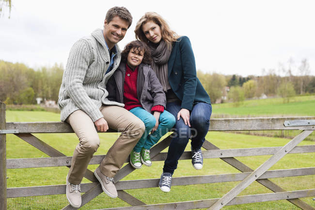 Portrait de garçon assis avec des parents sur une clôture en bois à la campagne — Photo de stock