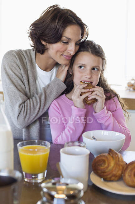 Fille prendre le petit déjeuner à côté de sa mère à un comptoir de cuisine — Photo de stock