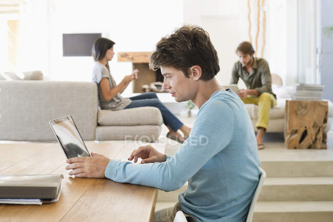 Людина використовує ноутбук зі своїми друзями, використовуючи електронні гаджети у фоновому режимі — стокове фото