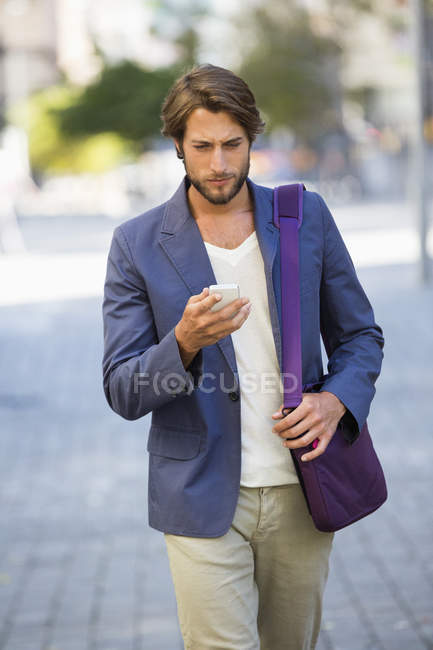 Giovane uomo d'affari che cammina per strada e utilizza un telefono cellulare — Foto stock