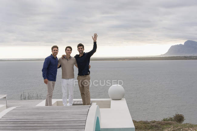 Portrait de trois heureux amis masculins debout au bord du lac — Photo de stock