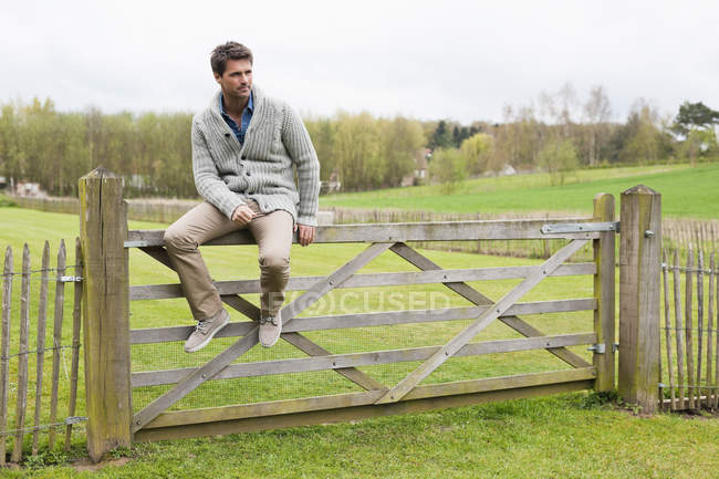 Homem sentado em cerca de madeira no campo e pensando — Fotografia de Stock