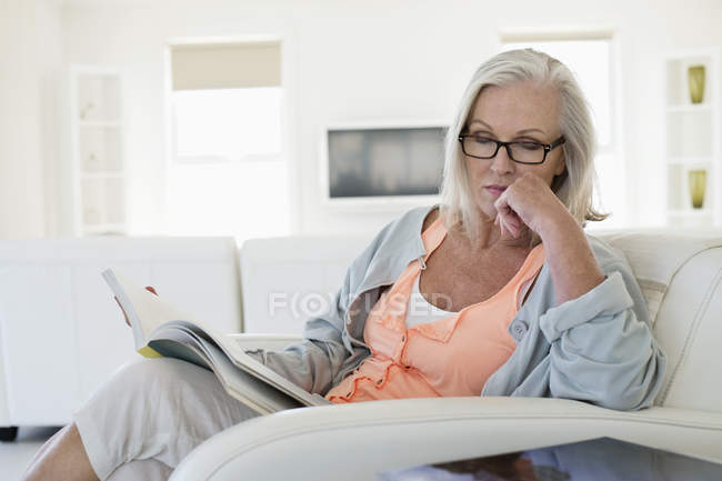 Mulher sentada no sofá e revista de leitura em casa — Fotografia de Stock