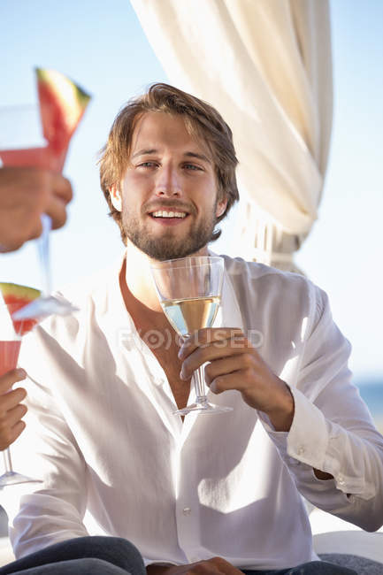 Homem sentado com amigos na costa e desfrutando de bebida — Fotografia de Stock