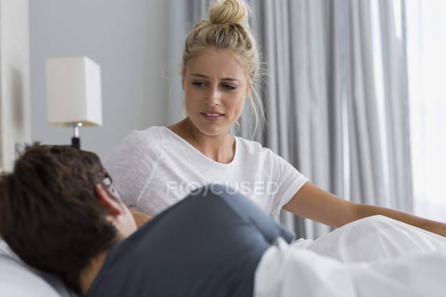 Молода жінка дивиться на чоловіка, який спить на ліжку — стокове фото