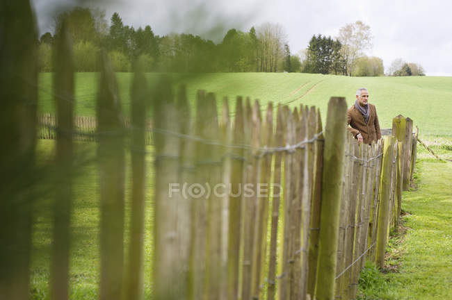 Чоловік стоїть біля паркану в зеленому полі — стокове фото