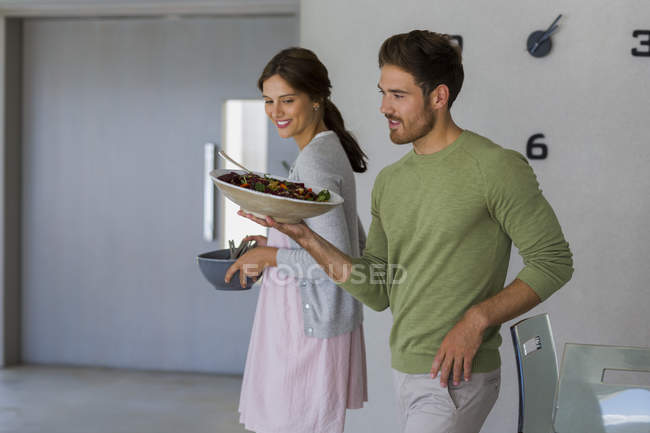 Young couple carrying food in bowls at home — Stock Photo