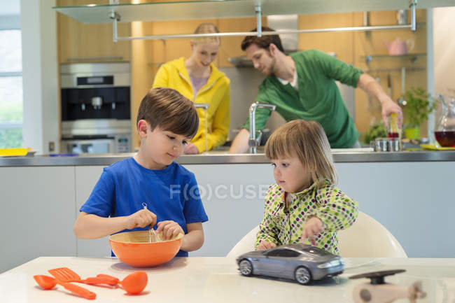 Niña con coche de juguete mirando hermano cocina en la cocina - foto de stock