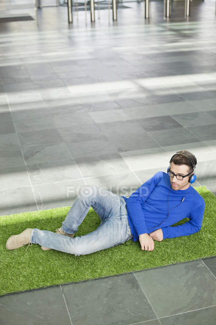 Businessman relaxing on fake grass and listening to music in office lobby — Stock Photo