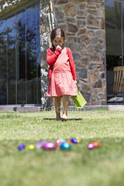 Дівчина дивиться на великодні яйця на зеленому газоні — стокове фото