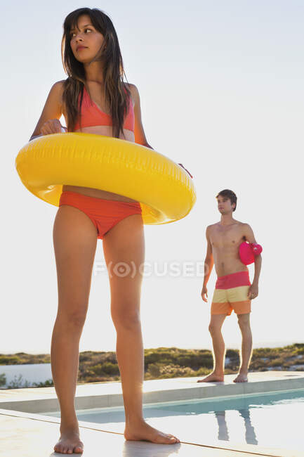 Женщина, идущая с надувным кольцом у бассейна с мужчиной позади нее — стоковое фото