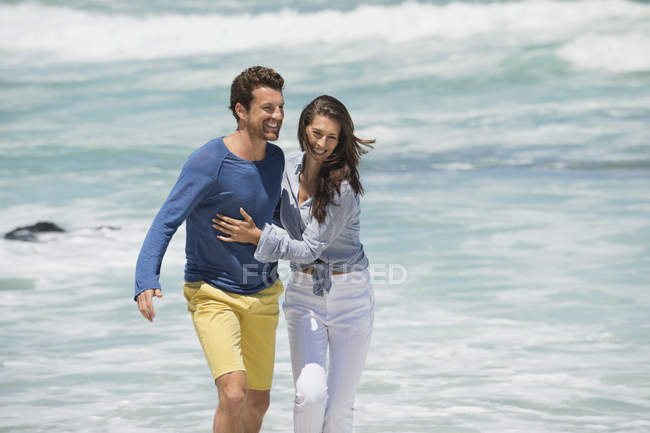 Пара прогулок по пляжу с волнистым морем на заднем плане и смотреть в камеру — стоковое фото